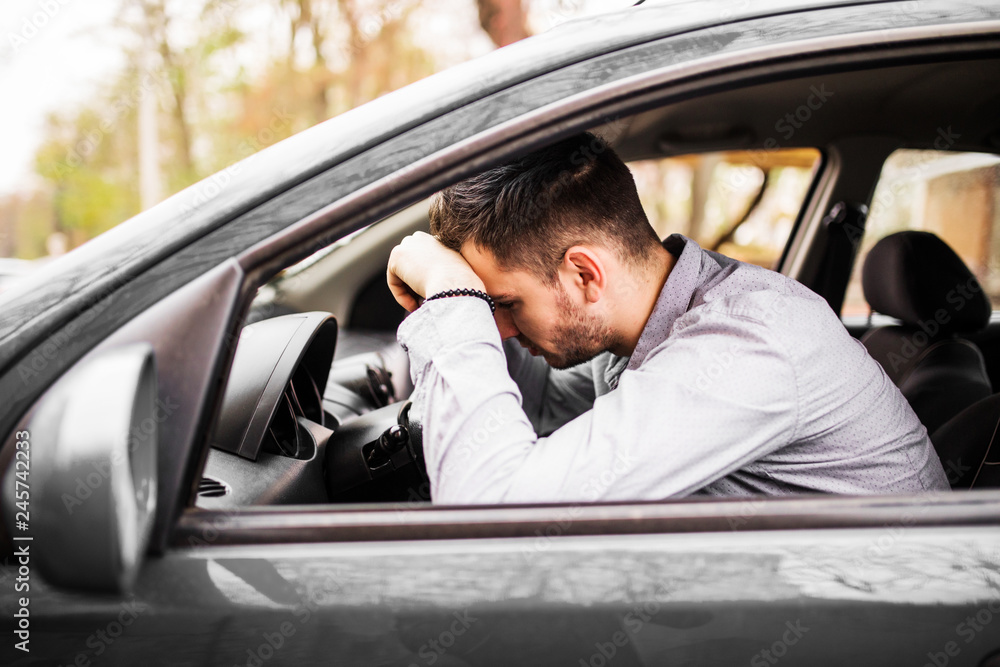 Young man sitting in car very upset and stressed after hard failure and moving in traffic jam