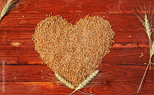 many Golden grains of wheat in the form of heart and ears lie on the backgrou...