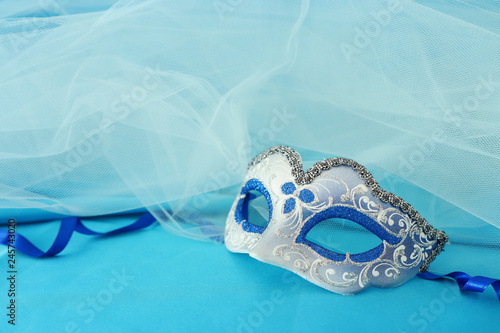 Photo of elegant and delicate silver and blue venetian mask over turquoise silk and chiffon background.