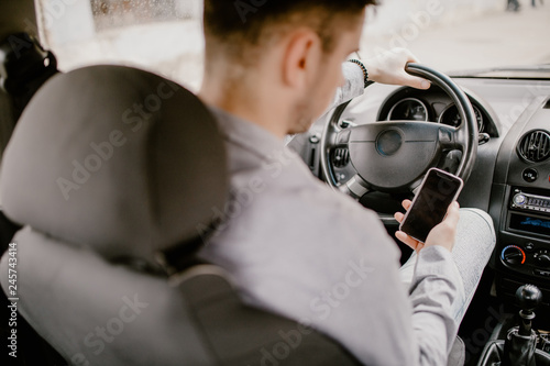 Man using a smart phone sitting on the front seat of the car.