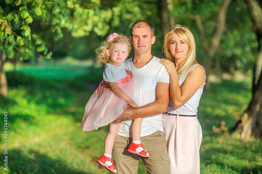 Naklejka premium Happy family in a beautiful spring park, dad holds a daughter in his arms, having fun and smiling, healthy outdoor recreation