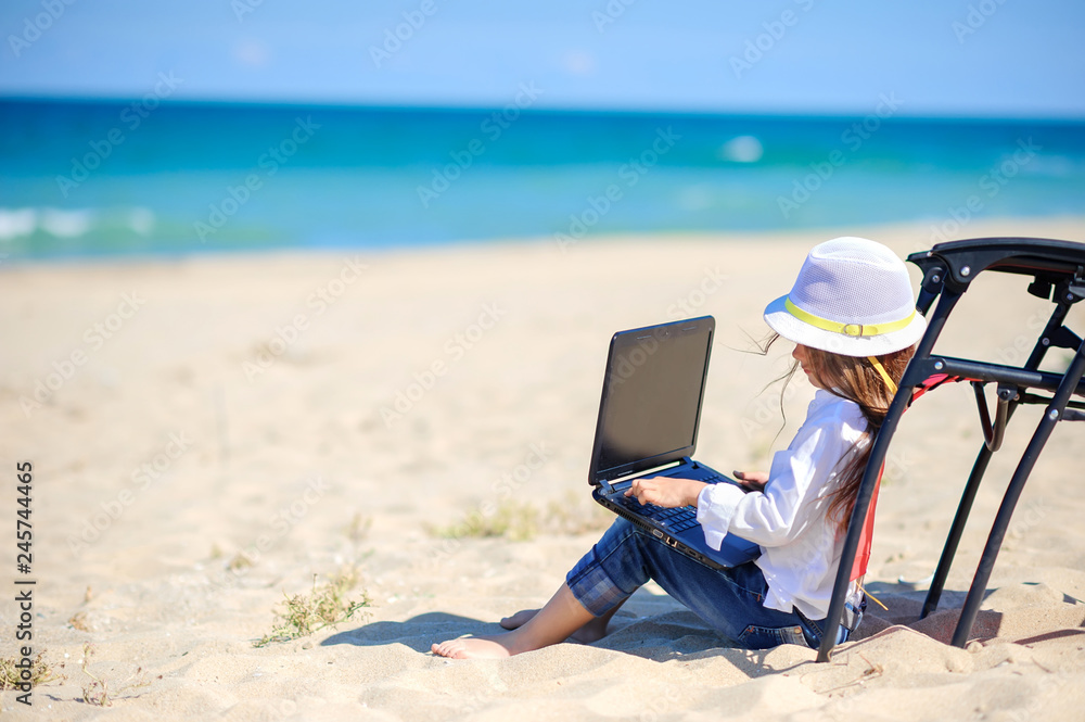 work in travel, girl teenager in a beach hat sitting near the beach chair with a laptop
