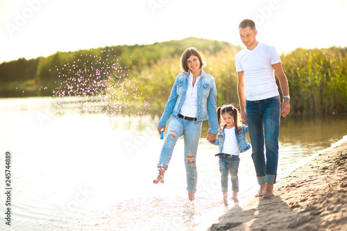 A happy family walks along the bank of the river in the evening, barefoot in the water and splashing, healthy outdoor recreation