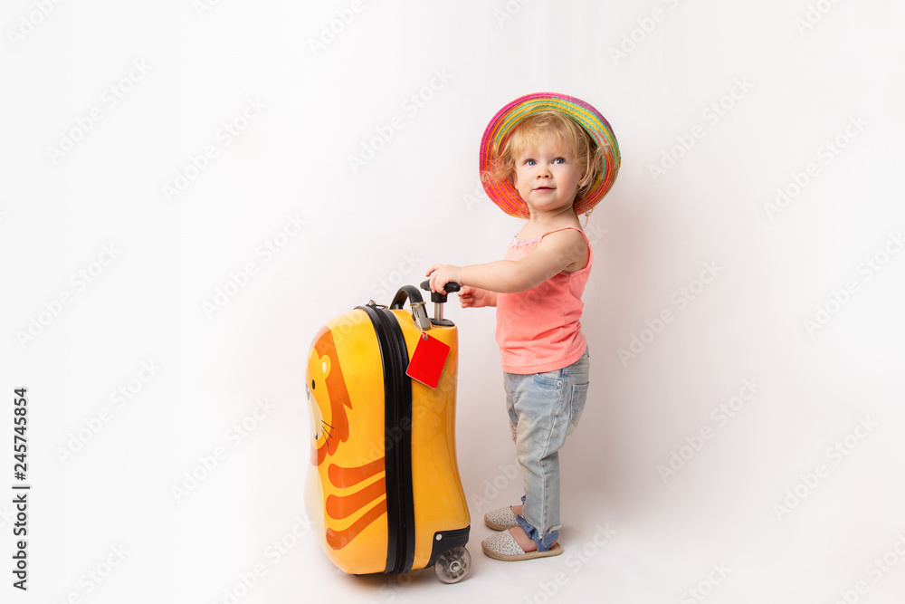 Funny curly little baby girl in a hat, T-shirt and jeans with a yellow suitcase is smiling on a white background waiting for an airplane. concept trip with kids Funny curly little baby girl in a hat, T-shirt and jeans with a yellow suitcase is smiling on a white background waiting for an airplane. concept trip with kids