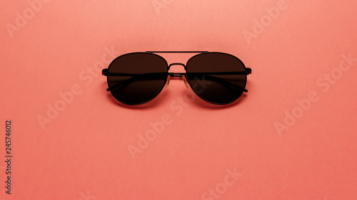 Black sunglasses on coral background. Top view. Flat lay. Copy space. New minimal creative concept. Summer is coming concept. Living Coral color of the Year 2019