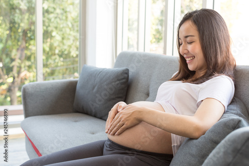 Attractive pregnant woman is sitting in sofa and holding her belly.