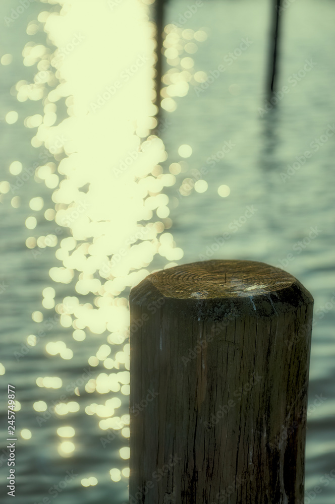 Wooden pole in the water with bright golden reflections and bokeh background blur.