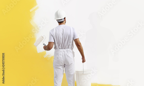 Rear view of painter man painting the wall, with paint roller and bucket, isolated on big empty copy space template photo