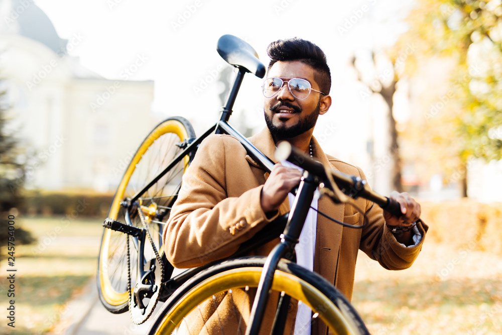 Bearded indian hipster man carrying bicycle on shoulder in the city
