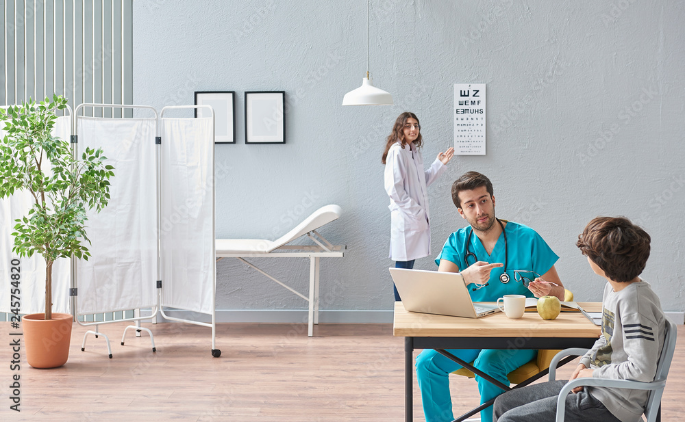 Obraz premium Ophthalmologist suggest wearing glasses for young boy in the health center. Modern office room for doctors.