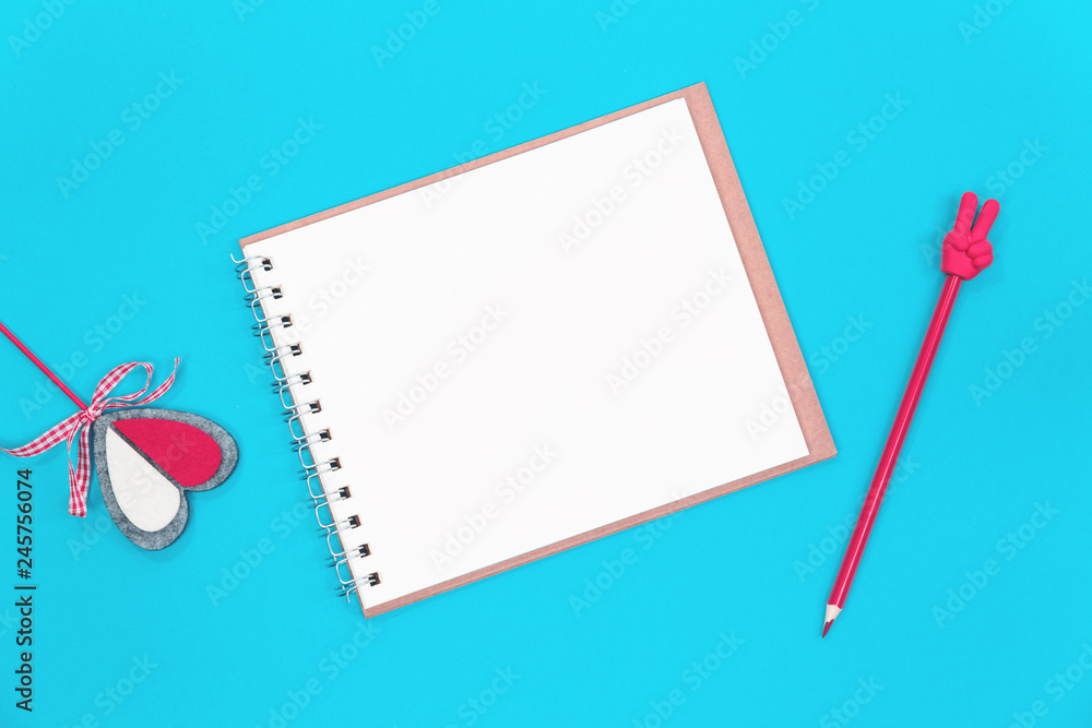 A red pencil with V sign, red crafted heart and a blank notepad on blue background. Flat lay with copy space A red pencil with V sign, red crafted heart and a blank notepad on blue background. Flat lay with copy space