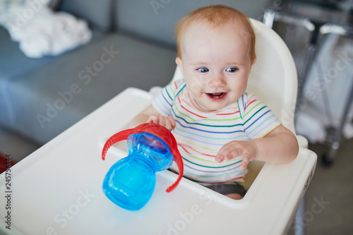 Little baby girl sitting in high chair and drinking water from sippy cup