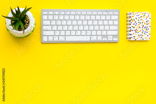Office workplace, work desk in office. Computer keyboard, glasses, stationery, plant on yellow background top view space for text