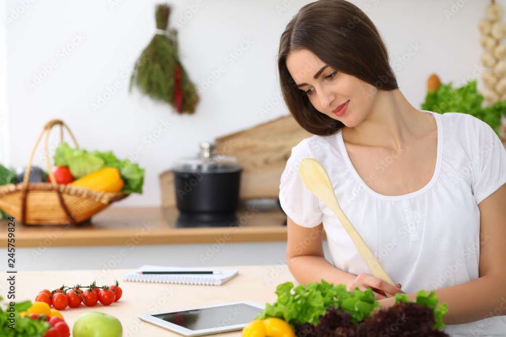 Beautiful Hispanic woman cooking while using tablet computer in kitchen or making online shopping by touchpad and credit card. Housewife found new recipe for dinner Beautiful Hispanic woman cooking while using tablet computer in kitchen or making online shopping by touchpad and credit card. Housewife found new recipe for dinner
