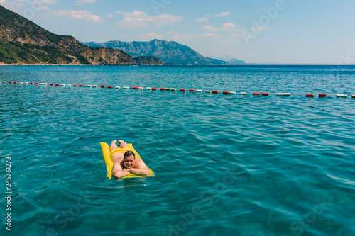 young adult man swimming on yellow inflatable mattress in blue sea.