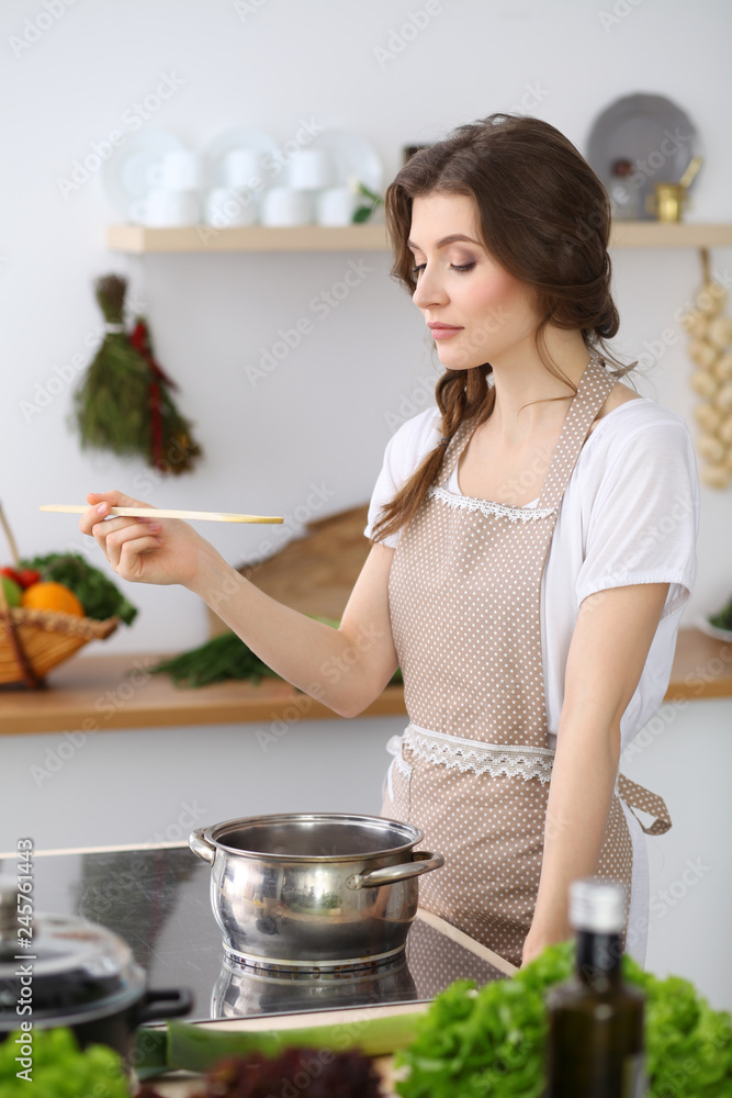 Young brunette woman cooking in kitchen. Housewife holding wooden spoon in her hand. Food and health concept