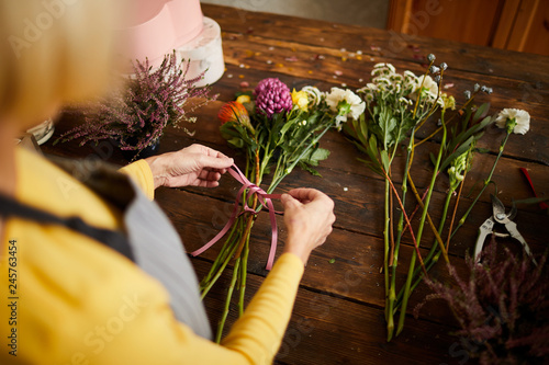 Bilde på lerret High angle closeup of unrecognizable female florist tying bouquet with ribbon wh