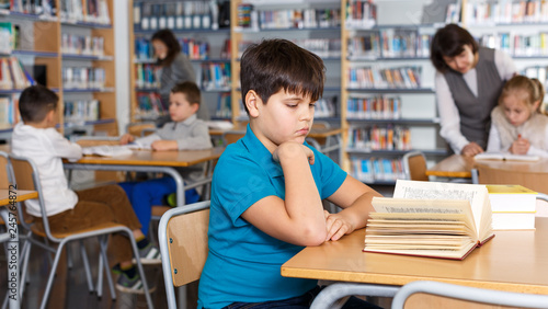 Tween boy reading textbooks in school library
