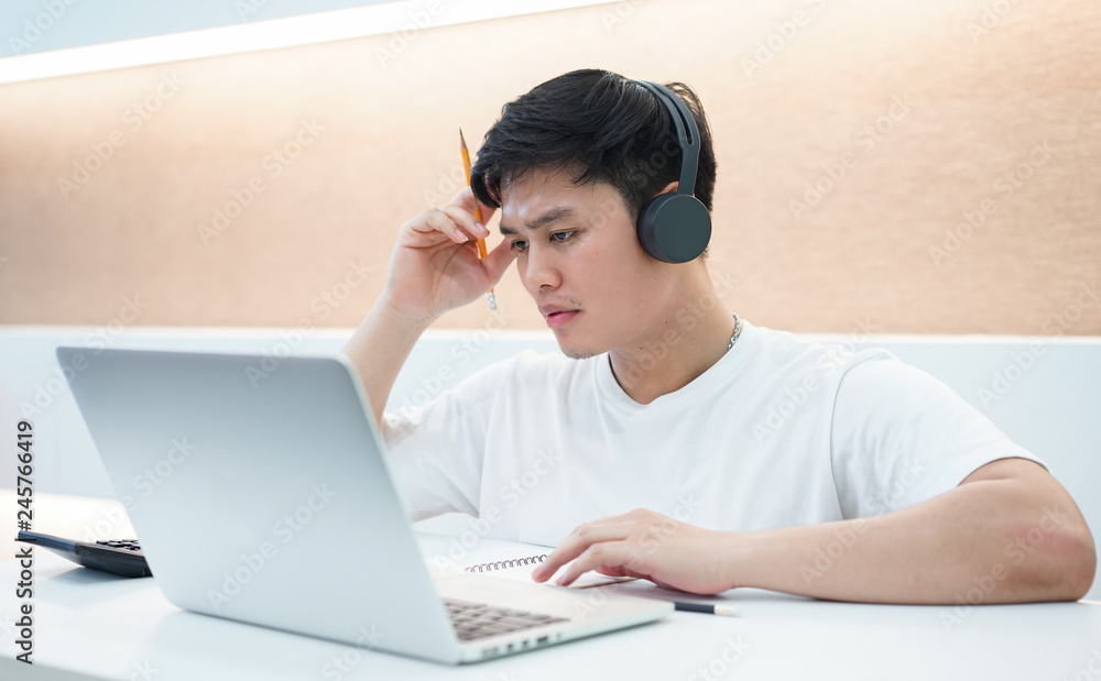 close up young asian student man wearing headset and looking at laptop display for learning mathematics online course from education website , writing lecture on notebook and solve lesson at library c close up young asian student man wearing headset and looking at laptop display for learning mathematics online course from education website , writing lecture on notebook and solve lesson at library c
