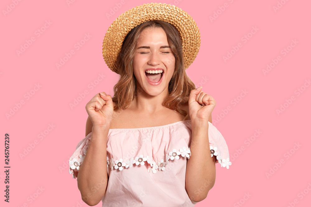 Isolated shot of overjoyed young woman clenches fists with happiness, closes eyes from pleasure, exclaims with triumph, wears fashionable clothes, isolated over pink background. Success concept Isolated shot of overjoyed young woman clenches fists with happiness, closes eyes from pleasure, exclaims with triumph, wears fashionable clothes, isolated over pink background. Success concept