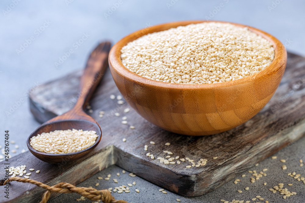 White sesame seeds in a wooden bowl and spoon. - obrazy, fototapety, plakaty 
