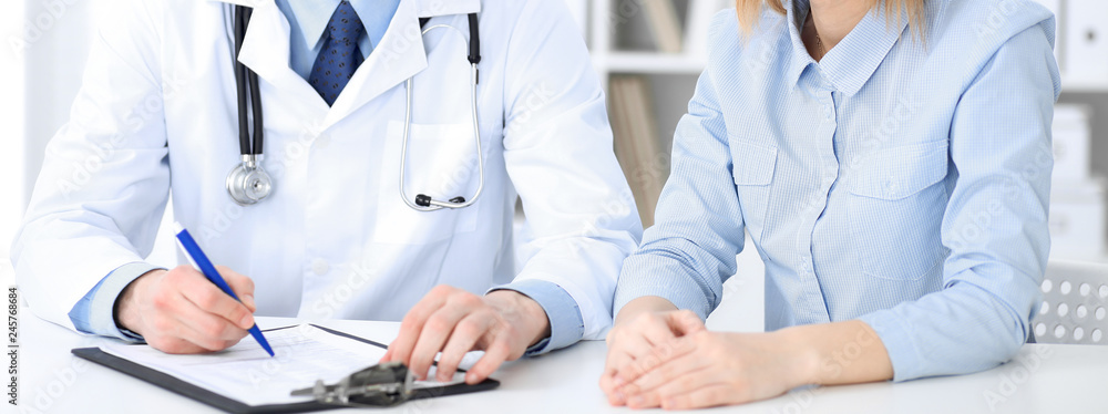 Doctor and patient sitting at the desk, close-up of unknown physician at work. Medicine and health care concept Doctor and patient sitting at the desk, close-up of unknown physician at work. Medicine and health care concept