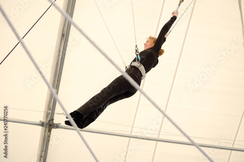 An adult female hangs on a flying trapeze at an indoor gym. The woman is an amateur trapeze artist. photo