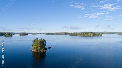 Aerial view of blue beautiful lake with islands and green forests on a sunny summer morning in Finland.