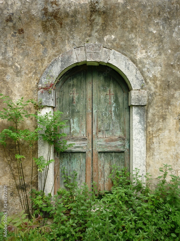 Entrance of old closed wooden door of an old abandoned christian orthodox church in a jungle surrounded by green plants Entrance of old closed wooden door of an old abandoned christian orthodox church in a jungle surrounded by green plants