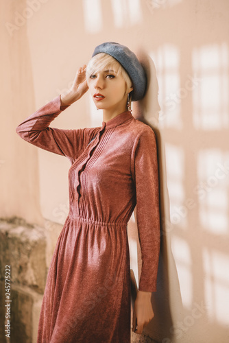Outdoor portrait of young beautiful fashionable woman wearing stylish pink dress, light blue beret, posing in street. Female spring fashion concept 
