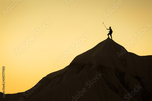 Landscape with a man in top of a peak taking a selfie with his phone on the stick at sunset.