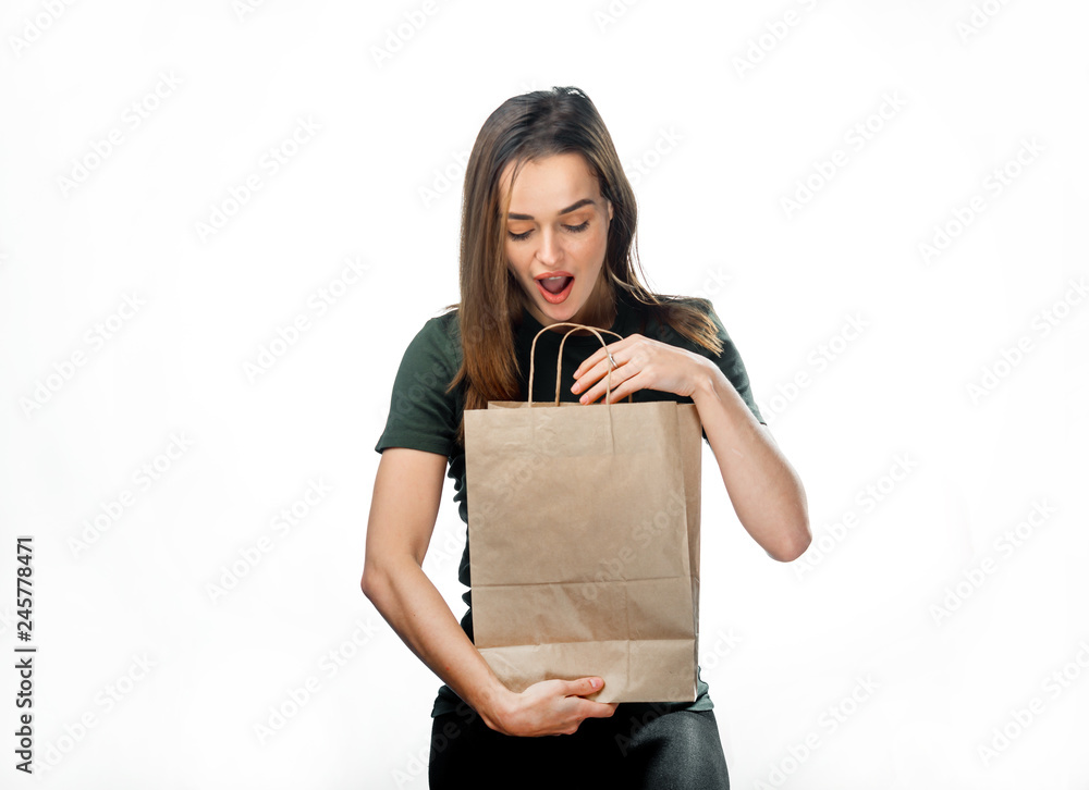 Fototapeta premium Portrait of surprised attractive long-haired woman looking into paper bag over the white background. Happy lady with surprise looks into a paper bag