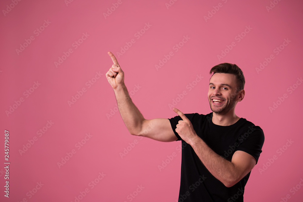Happy handsome young man portrait in black t-shirt isolated on pink wall