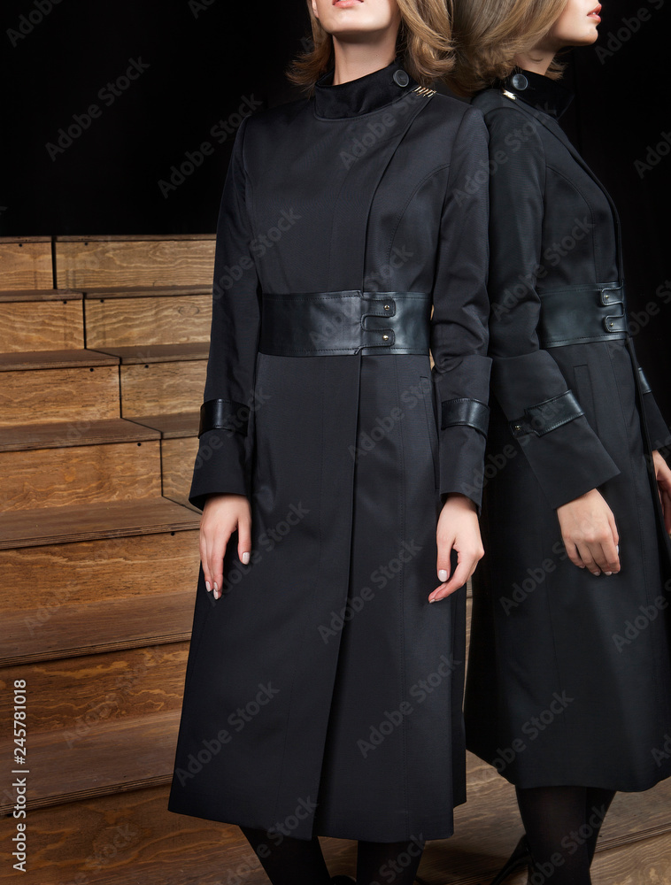 Woman in coat and photomodel posing. Wooden floor and stairs. Black background with mirror and reflection. Fashion and design, luxury. Woman in coat and photomodel posing. Wooden floor and stairs. Black background with mirror and reflection. Fashion and design, luxury.