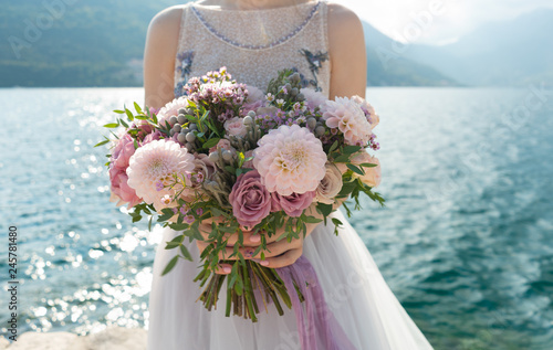 the bride holds a pink and lilac wedding bouquet in her arms against the background of the sea photo