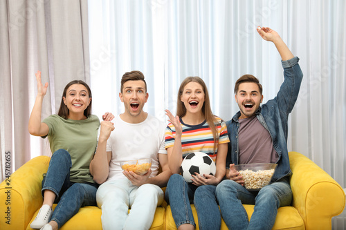Group of people with snacks and ball watching soccer match on TV at home
