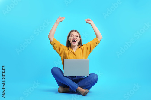 Emotional young woman with laptop celebrating victory on color background © New Africa