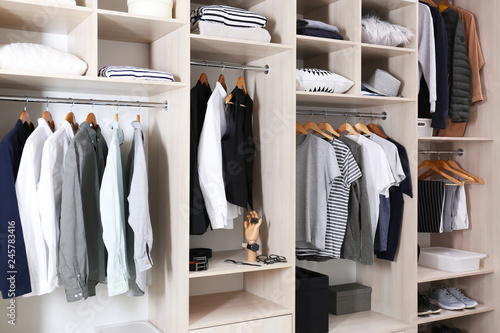 Photo Stylish clothes, shoes and home stuff in large wardrobe closet