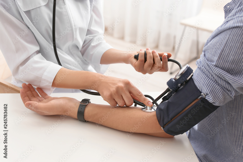Doctor checking patient's blood pressure in hospital, closeup. Cardiology concept