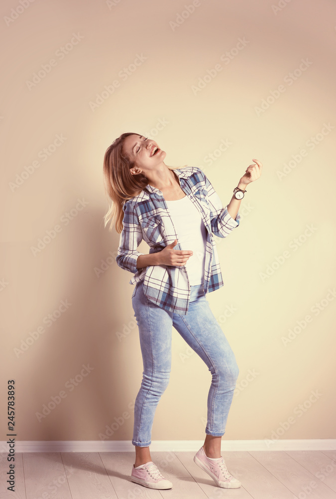 Young woman playing air guitar near grey wall