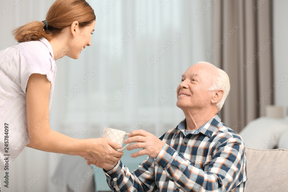 Obraz premium Elderly man taking cup of tea from female caregiver at home
