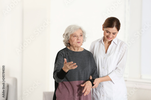 Elderly woman with caregiver indoors. Space for text
