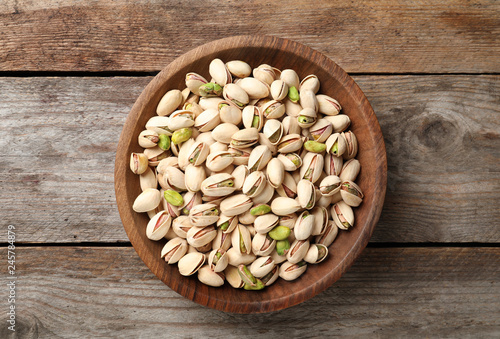 Organic pistachio nuts in bowl on wooden table, top view