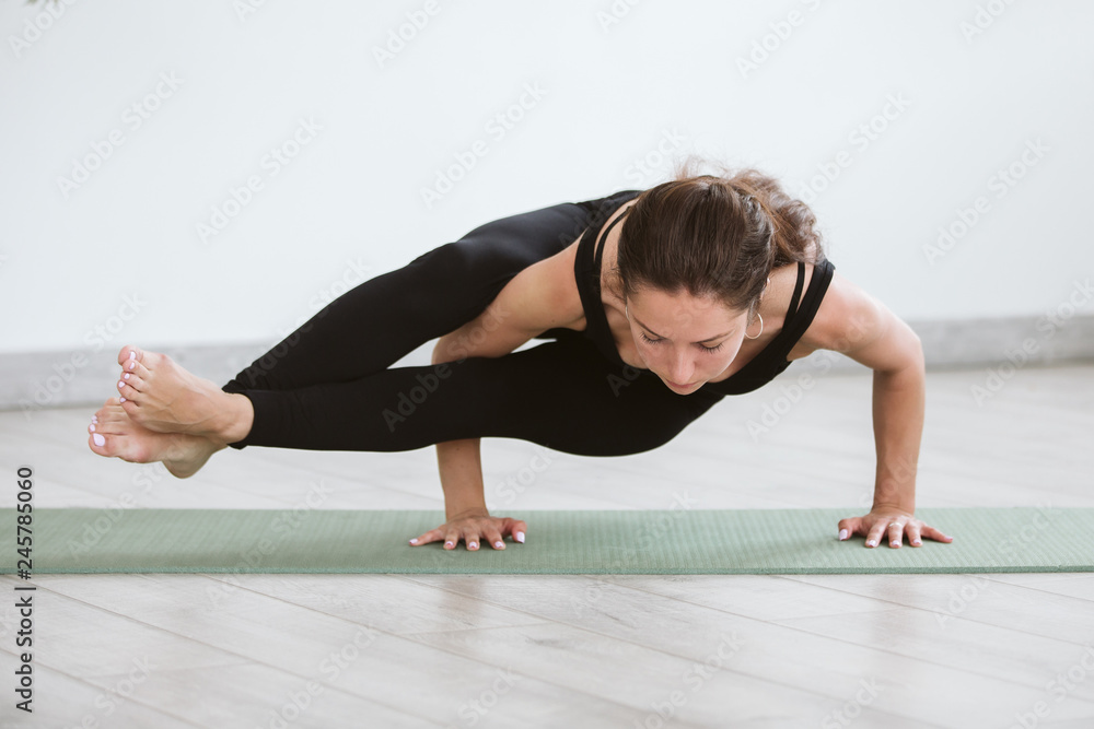 Fototapeta premium Yoga and Fitness. Young woman sitting in Astavakrasana yoga pose at home