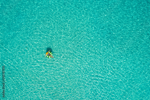Aerial view of slim woman swimming on the swim ring  donut in the transparent turquoise sea in Seychelles. Summer seascape with girl, beautiful waves, colorful water. Top view from drone © gawriloff