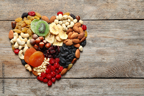 Heart made of different dried fruits and nuts on wooden background, top view. Space for text
