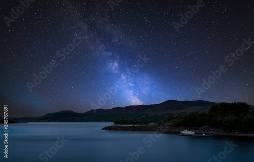 Stunning vibrant Milky Way composite image over landscape of calm lake with boat on shore © veneratio