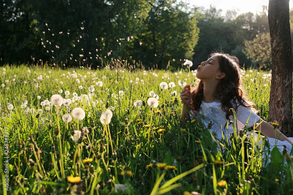 Teen blowing seeds from a dandelion flower in a spring park Teen blowing seeds from a dandelion flower in a spring park