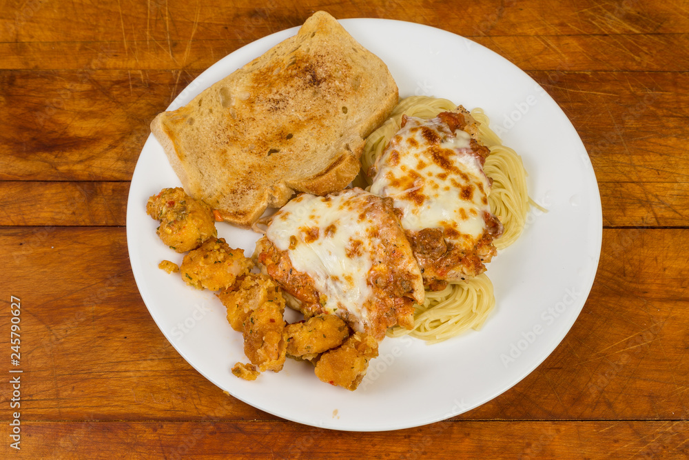 Chicken Parmigiana and Shrimp Scampi Fritta on white plate against rustic wooden table Chicken Parmigiana and Shrimp Scampi Fritta on white plate against rustic wooden table