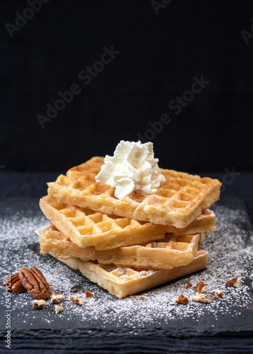 Close-up of sweet tasty Belgian waffles, sprinkled with powdered sugar, pecans, with whipped cream